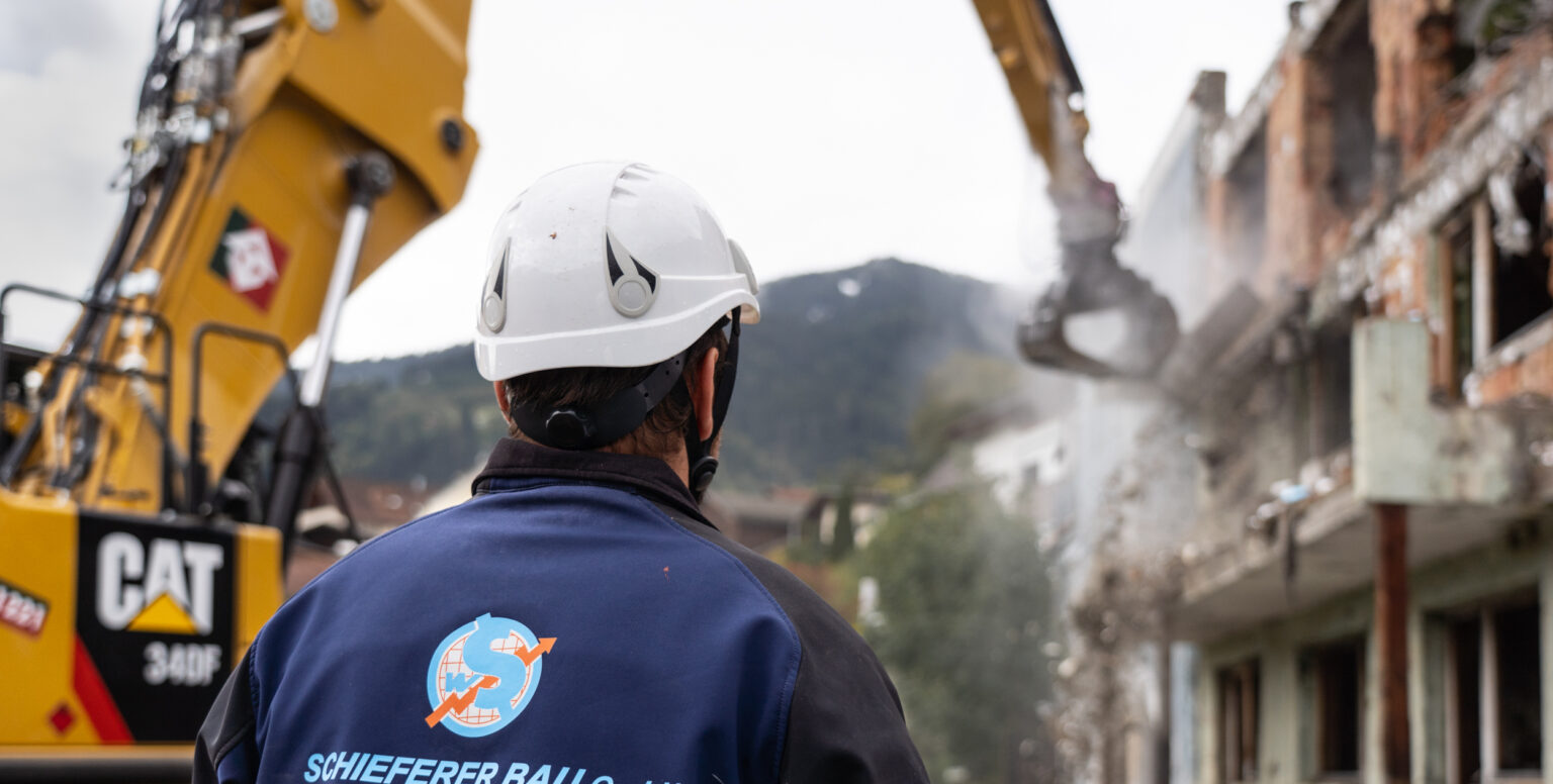 Mitarbeiter vor einem Kran, der ein Haus abreißt